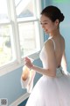 A woman in a white dress holding a pair of ballet shoes.