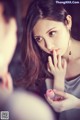 A woman holding a pink lipstick in front of a mirror.