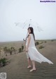 A woman in a white dress holding an umbrella in the sand.