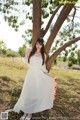 A woman in a white dress standing under a tree.