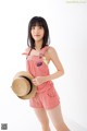 A woman in a red and white striped romper holding a straw hat.