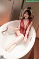 A woman in a red lingerie sitting in a bathtub.