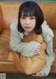 A woman sitting on a brown couch holding a brown pillow.