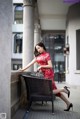 A woman in a red dress sitting on a chair.